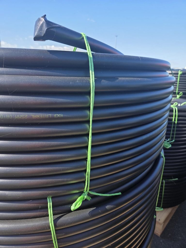 Coiled black irrigation tubing secured with bright green straps outdoors.
